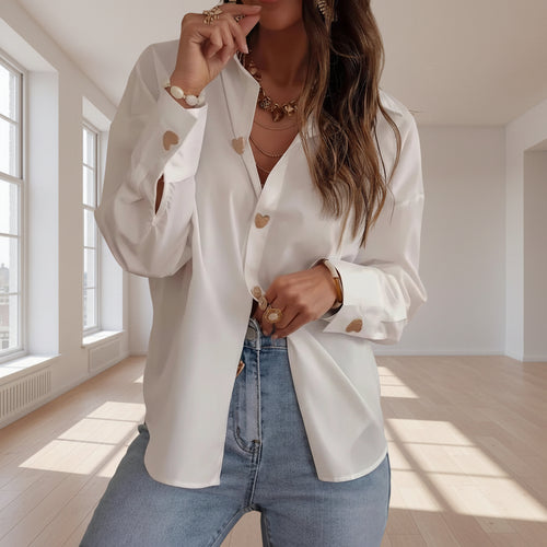 Woman wearing a white blouse with heart patterns and blue jeans indoors.
