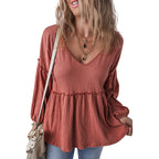 Woman wearing a rust-colored blouse with long sleeves and layered design on a white background