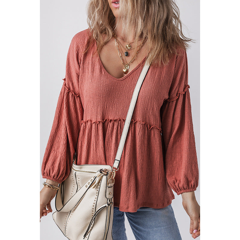 Woman wearing a rust-colored blouse with long sleeves and a white handbag on a plain background