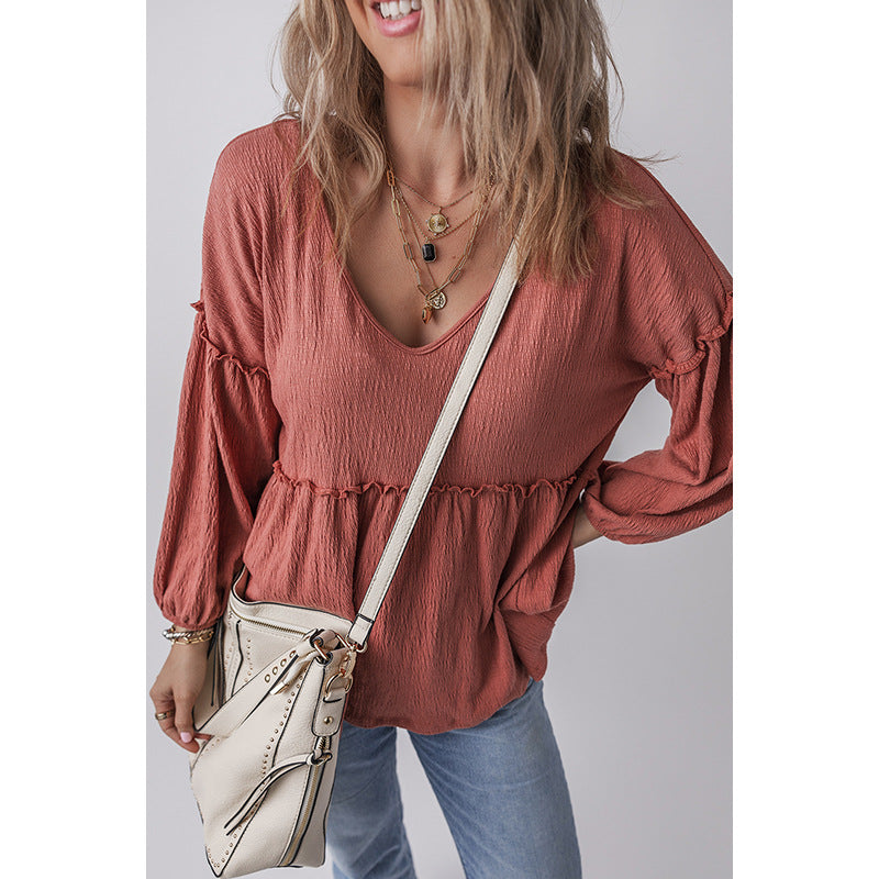 Woman wearing a rust-colored blouse with long sleeves, holding a beige handbag against a plain background.