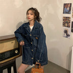 Woman wearing a denim jacket standing next to a vintage radio in a room with posters on the wall.