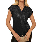 Woman wearing a black sequin top holding a beige clutch against a white background