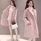 Woman wearing a pink coat with fur lining, holding a black and white handbag on a plain background.