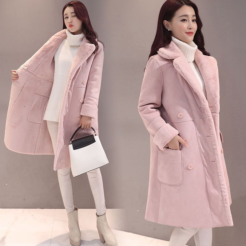Woman wearing a pink coat with fur lining, holding a black and white handbag on a plain background.