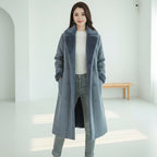 Woman wearing a long gray coat in a room with a couch and table.