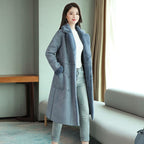 Woman wearing a long gray coat in a room with a couch and table.