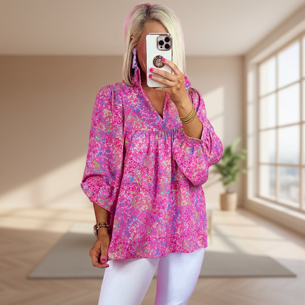 Woman taking a mirror selfie wearing a pink floral blouse against a pink background