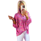 Woman wearing a pink floral blouse and white pants, taking a mirror selfie.