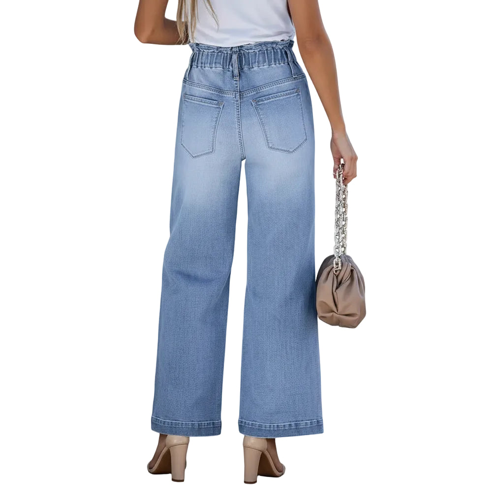 Person wearing light blue wide-leg jeans holding a beige handbag against a plain background