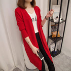 Person wearing a red cardigan over a white shirt with text, standing in a room.