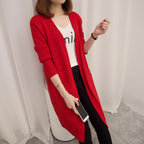 Person wearing a red cardigan over a white shirt with text, standing in a room.