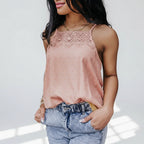 Woman wearing a pink lace top and blue jeans standing indoors with plants in the background