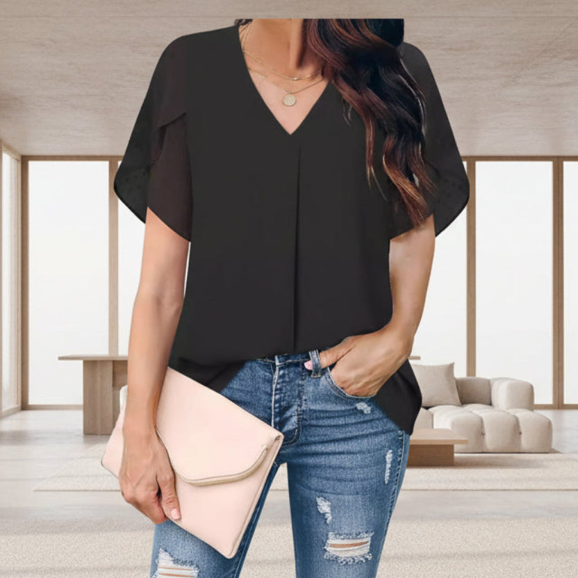 Woman wearing a black blouse and blue jeans, holding a beige clutch.