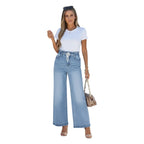 Woman wearing a white top and light blue jeans standing against a white wall.