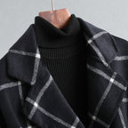 Black turtleneck sweater with a plaid scarf draped over it on a wooden hanger against a gray background.