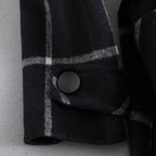 Close-up of a black and gray checkered coat with a button on a light gray background