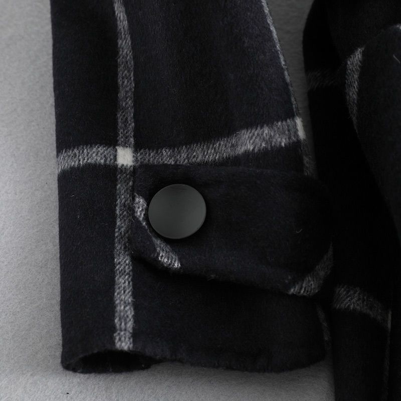 Close-up of a black and gray checkered coat with a button on a light gray background