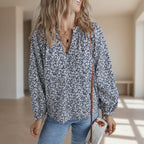 Woman wearing a floral blouse and holding a small bag against a plain background