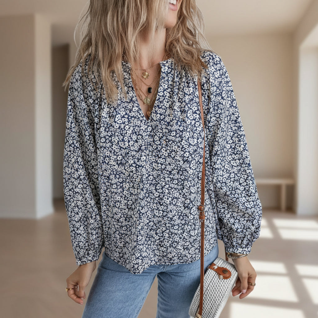 Woman wearing a floral blouse and holding a small bag against a plain background