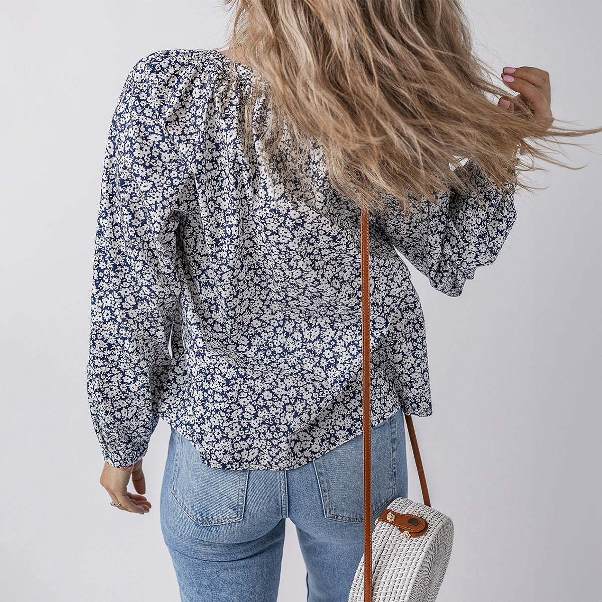 Person wearing a floral blouse and jeans, holding a straw bag against a plain background