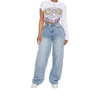 Person wearing a white long-sleeve crop top with a graphic design and light blue jeans on a plain background