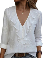 White blouse with ruffled details and floral embroidery on a blurred background