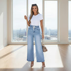 Woman wearing a white top and light blue jeans standing against a white wall.
