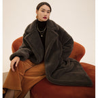 Woman wearing a dark gray coat sitting on an orange couch in a warm-toned room.