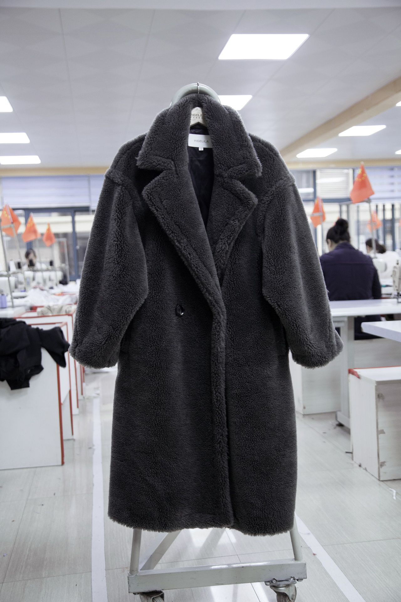 Dark gray coat on a hanger in an indoor setting with tables and chairs.