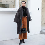 Woman wearing a long gray coat and brown skirt in front of a white building.