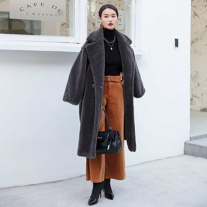 Woman wearing a long gray coat and brown skirt in front of a white building.